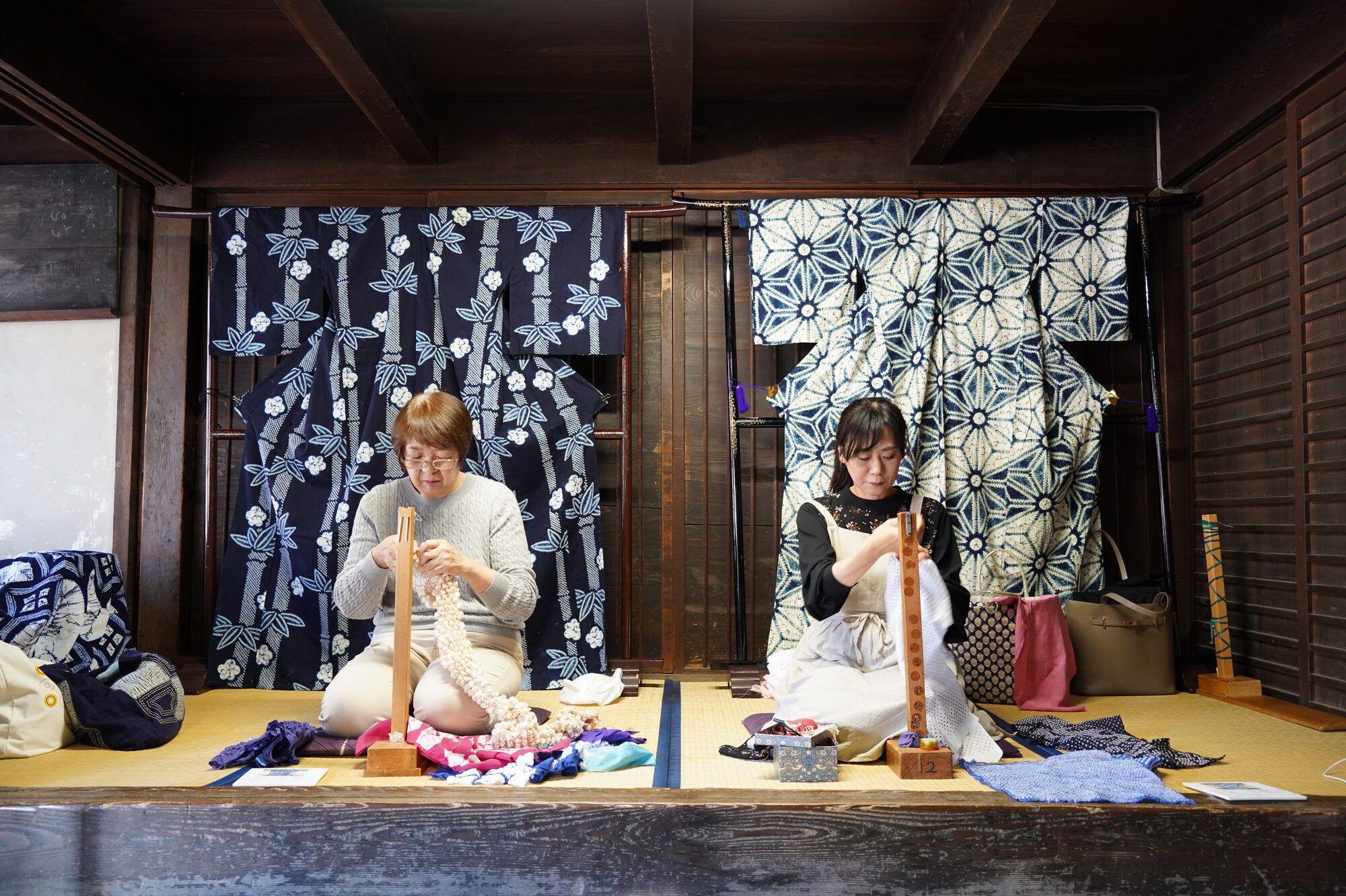 町家の座敷で布を糸でくくり、絞りの模様を生み出す職人の手元。